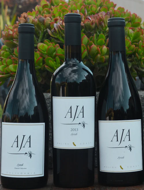 Three library vintages of AJA Syrah standing in front of the vineyard